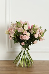 Beautiful bouquet of fresh flowers on wooden table near white wall