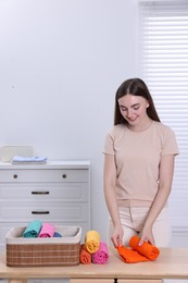 Photo of Young woman rolling shirt at table in room. Organizing clothes