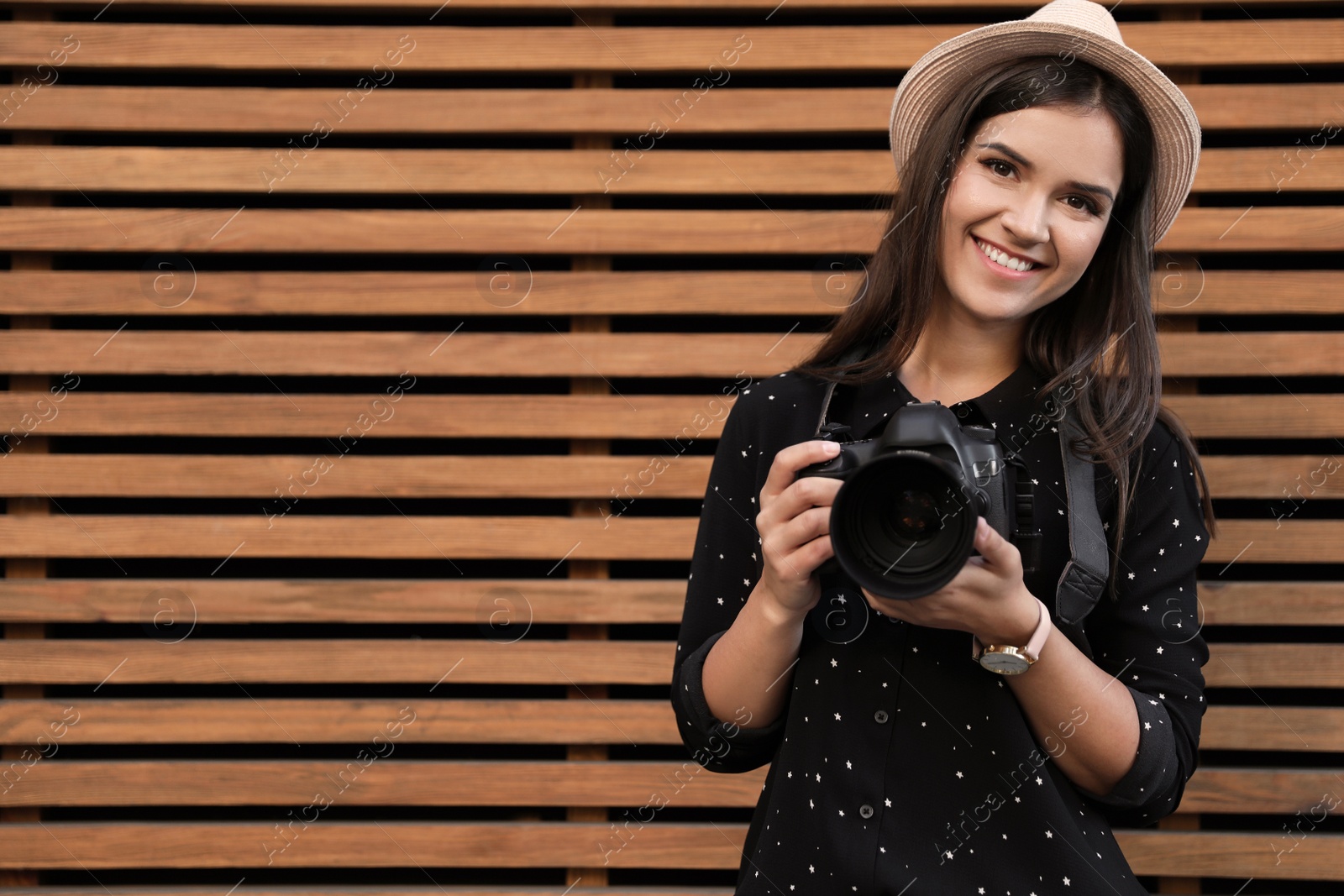 Photo of Young female photographer with professional camera near wooden wall. Space for text
