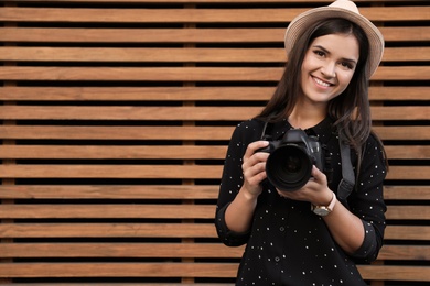 Young female photographer with professional camera near wooden wall. Space for text