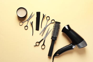 Photo of Scissors and other hairdresser's accessories on light yellow background, flat lay