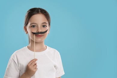 Photo of Cute little girl with fake mustache on turquoise background, space for text