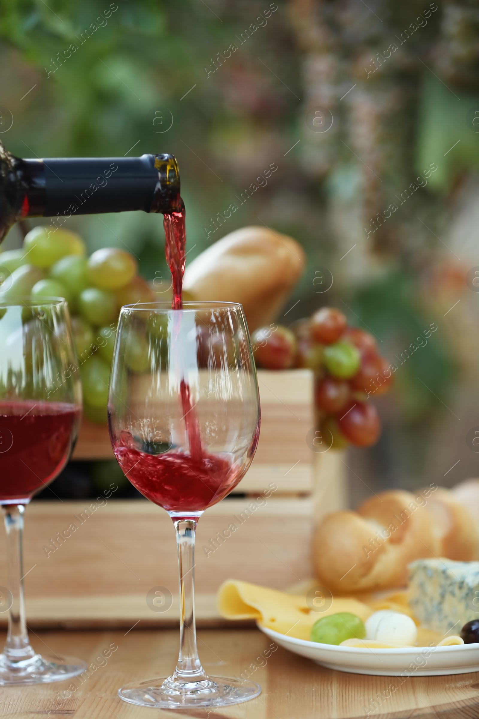 Photo of Pouring red wine from bottle into glass on table in vineyard