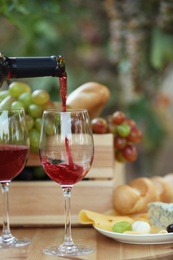 Pouring red wine from bottle into glass on table in vineyard