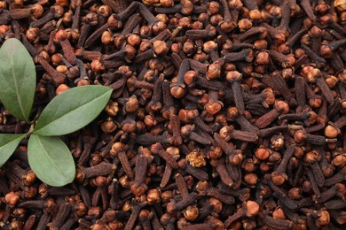 Many aromatic cloves and green leaves as background, top view. Space for text