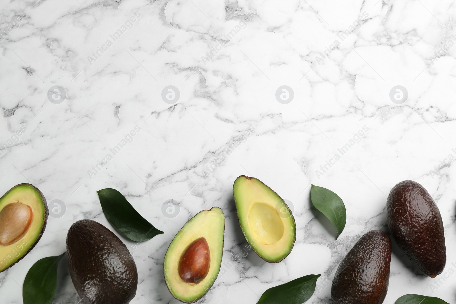 Photo of Whole and cut avocados with green leaves on white marble table, flat lay. Space for text
