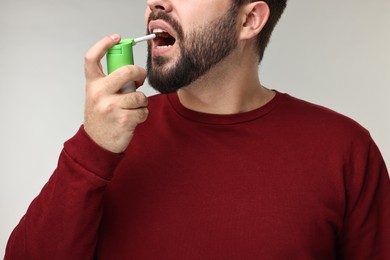 Photo of Young man using throat spray on grey background, closeup