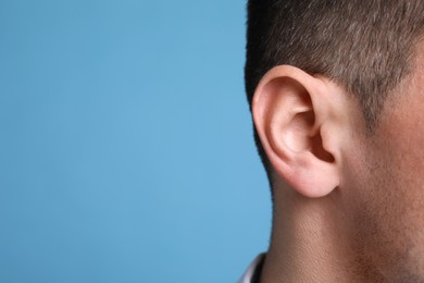 Photo of Man on light blue background, closeup of ear. Space for text