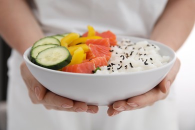 Woman holding delicious poke bowl with rice, salmon and vegetables, closeup