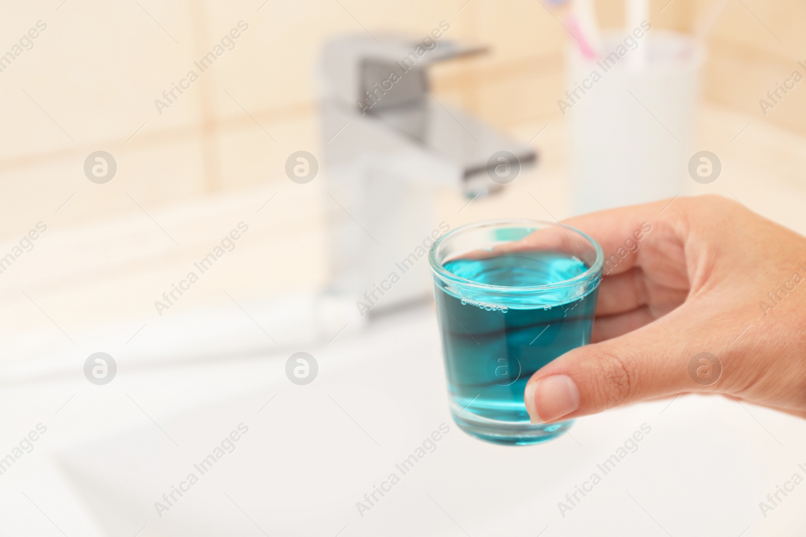 Photo of Woman holding glass with mouthwash for teeth and oral care in bathroom