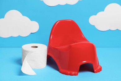 Red baby potty and bog roll against light blue background with paper clouds. Toilet training
