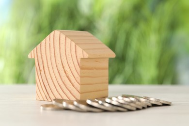 Wooden house model and coins on light table outdoors