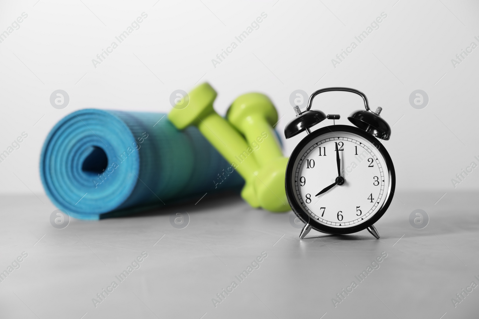 Photo of Alarm clock, yoga mat and dumbbells on grey background. Morning exercise