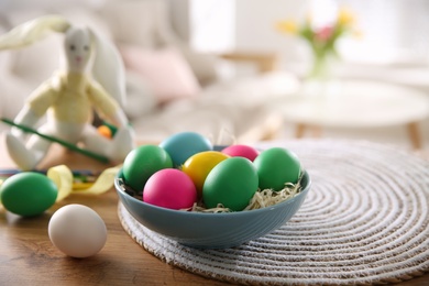 Photo of Bright painted Easter eggs in bowl on wooden table indoors, space for text