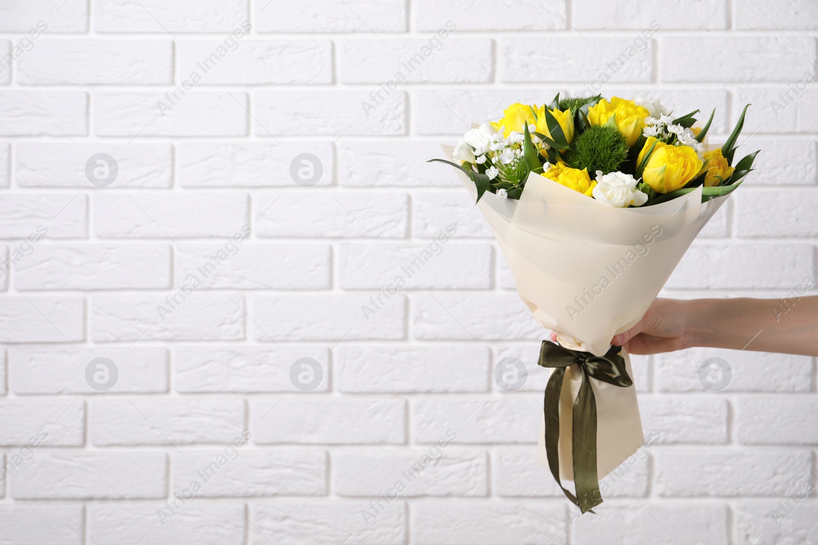 Photo of Woman with bouquet of beautiful tulips near white brick wall, closeup. Space for text