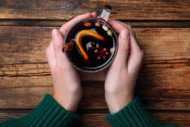 Woman with cup of mulled wine at wooden table, top view