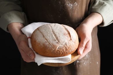 Woman holding freshly baked bread on black background, closeup