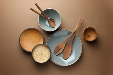 Stylish empty dishware and wooden cutlery on brown background, flat lay