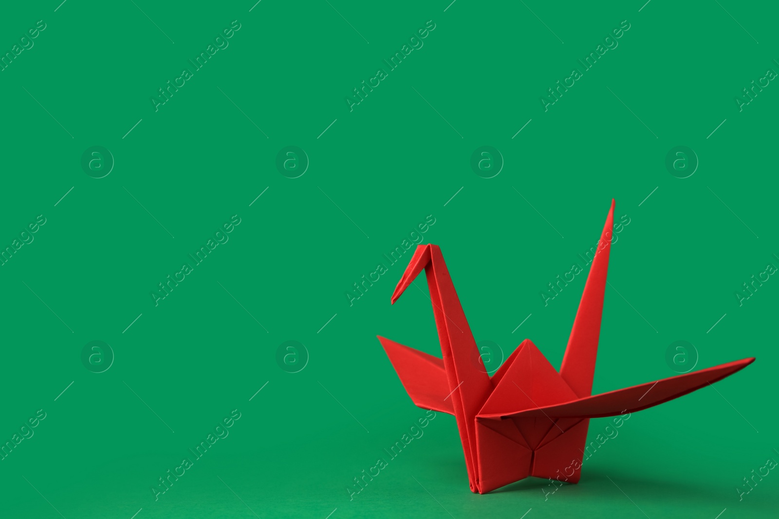 Photo of Red paper origami crane on green background, space for text