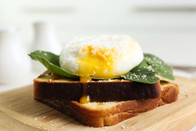 Photo of Delicious poached egg with toasted bread and spinach served on wooden board, closeup