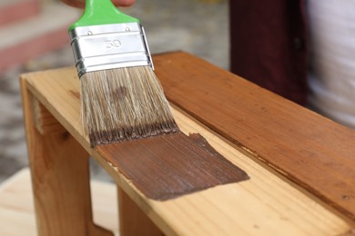 Photo of Man applying wood stain onto crate against blurred background, closeup