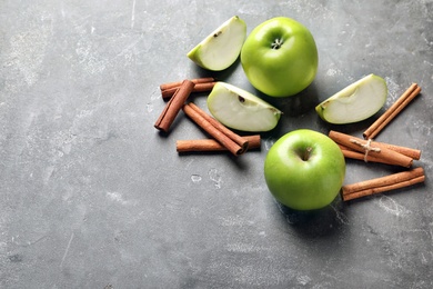 Fresh apples and cinnamon sticks on gray table