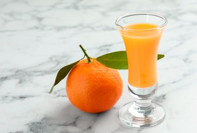 Photo of Delicious tangerine liqueur in shot glass and fresh fruit on white marble table, closeup