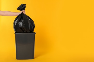 Photo of Woman holding trash bag full of garbage over bucket on orange background, closeup. Space for text