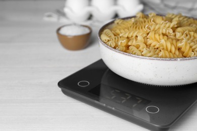 Photo of Electronic scales with uncooked pasta on white wooden table, closeup. Space for text