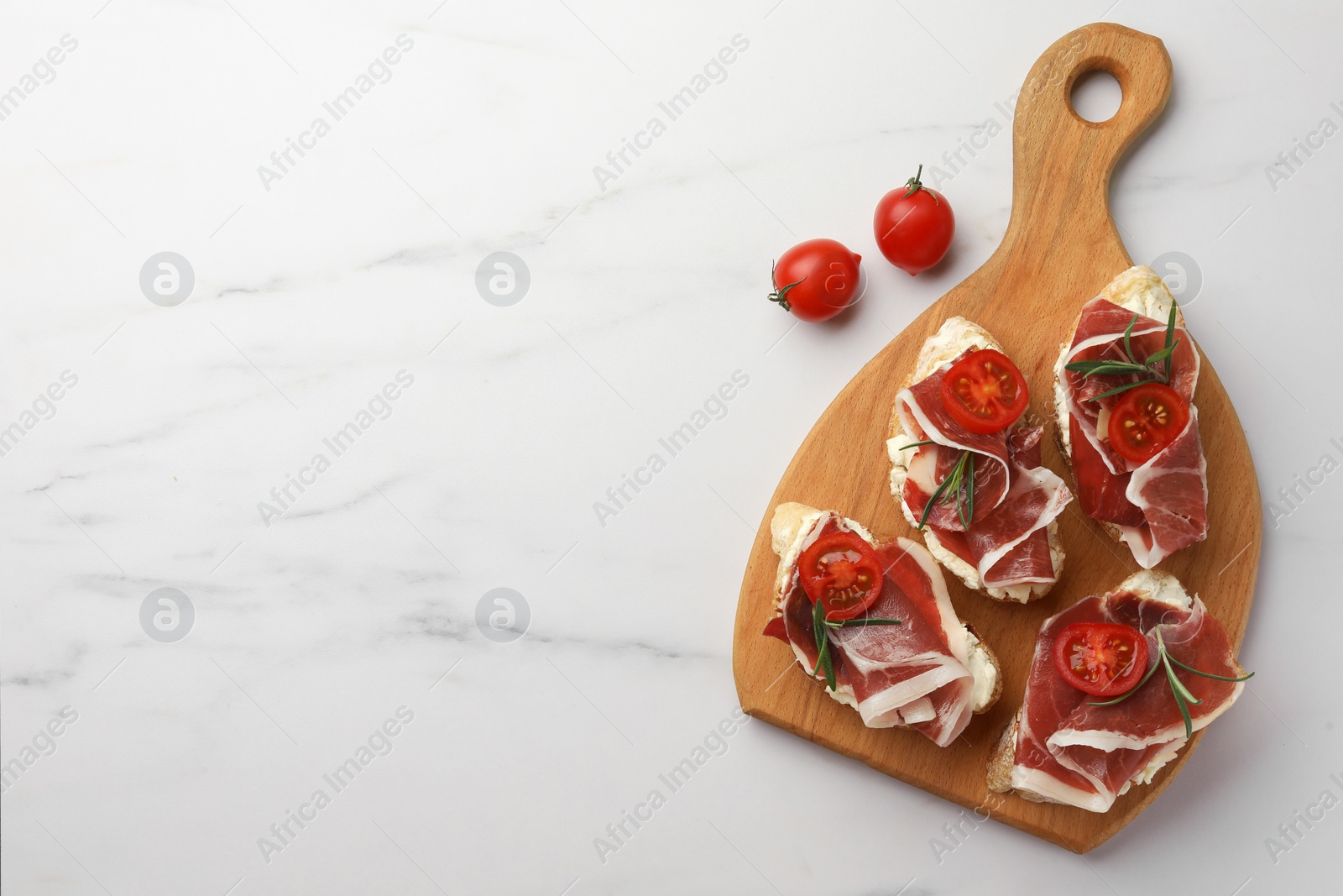 Photo of Tasty sandwiches with cured ham, rosemary and tomatoes on white marble table, flat lay. Space for text