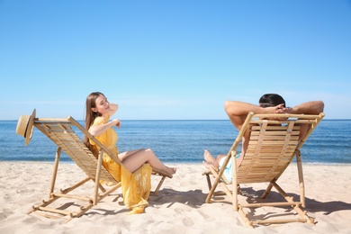 Photo of Woman and her boyfriend on deck chairs at beach. Happy couple