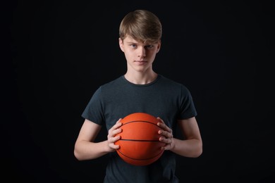 Teenage boy with basketball ball on black background