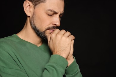 Photo of Man with clasped hands praying on black background, closeup