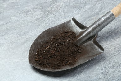 Photo of Metal shovel with fertile soil on gray textured surface