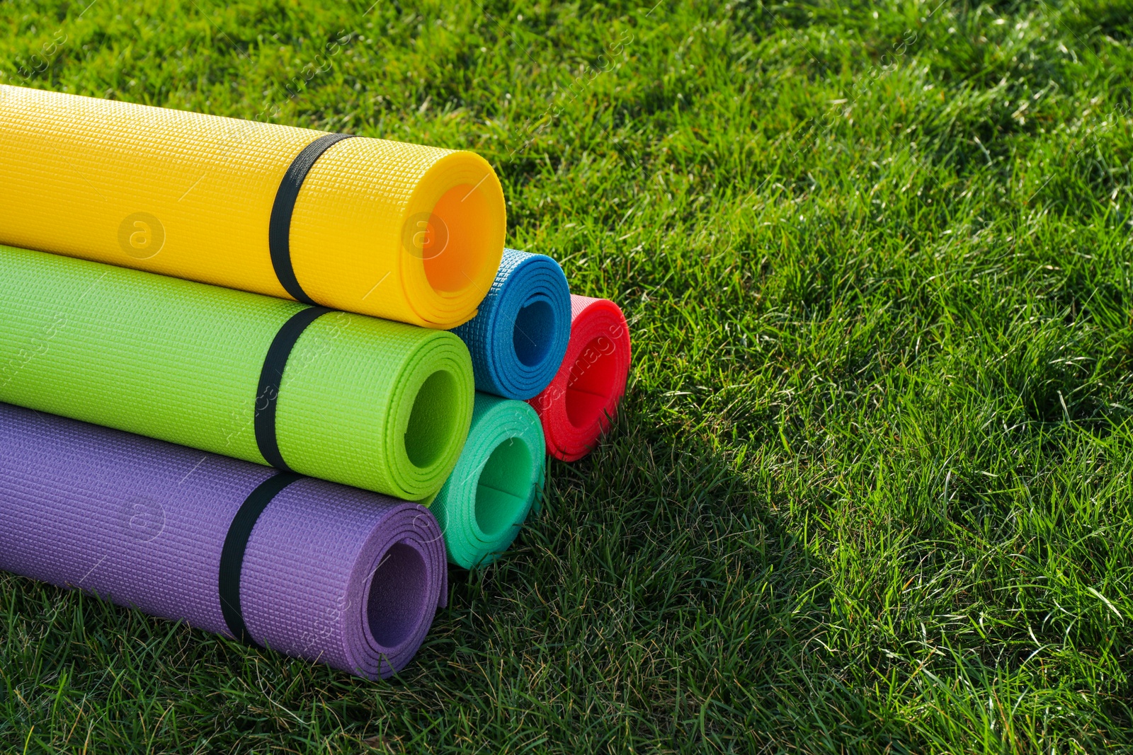 Photo of Bright exercise mats on fresh green grass outdoors, space for text