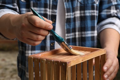 Photo of Man applying varnish onto wooden crate against blurred background, closeup