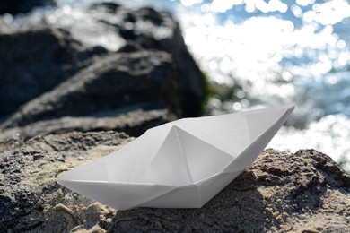 Photo of White paper boat on rock near sea, closeup