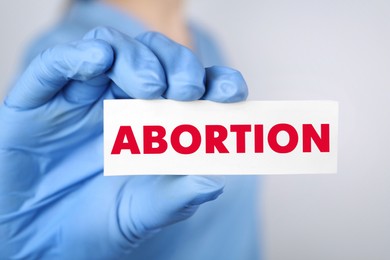 Image of Doctor holding paper card with word Abortion on light grey background, closeup
