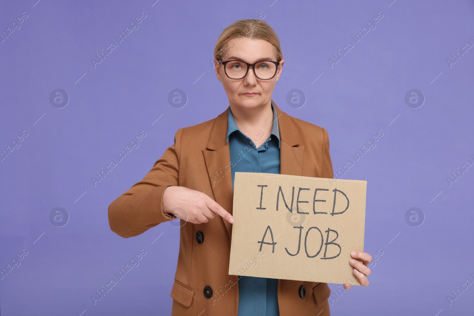 Photo of Unemployed senior woman pointing at cardboard sign with phrase I Need A Job on purple background