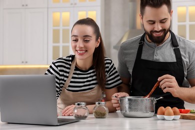 Happy lovely couple using laptop while cooking in kitchen