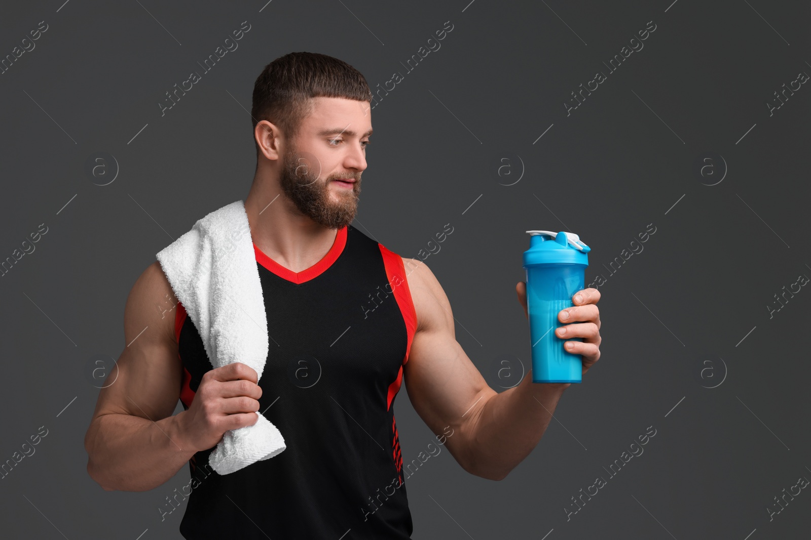 Photo of Young man with muscular body holding shaker of protein and towel on grey background