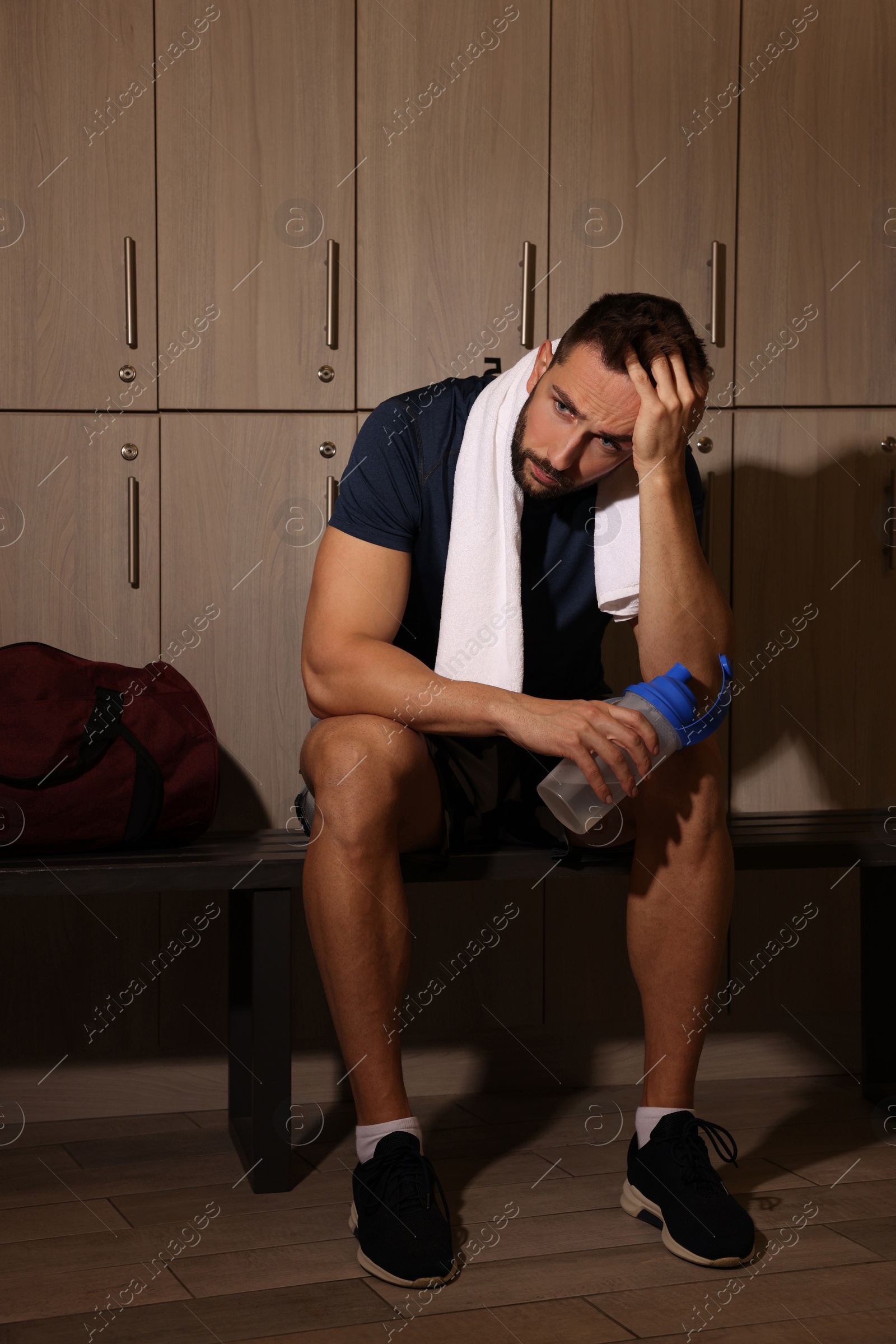 Photo of Handsome tired man with shaker in locker room