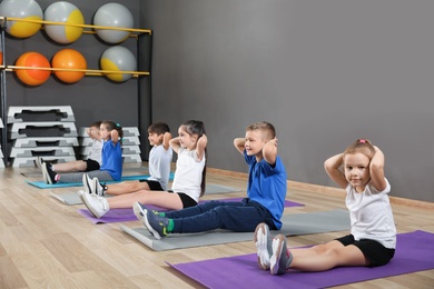 Photo of Cute little children sitting on floor and doing physical exercise in school gym. Healthy lifestyle