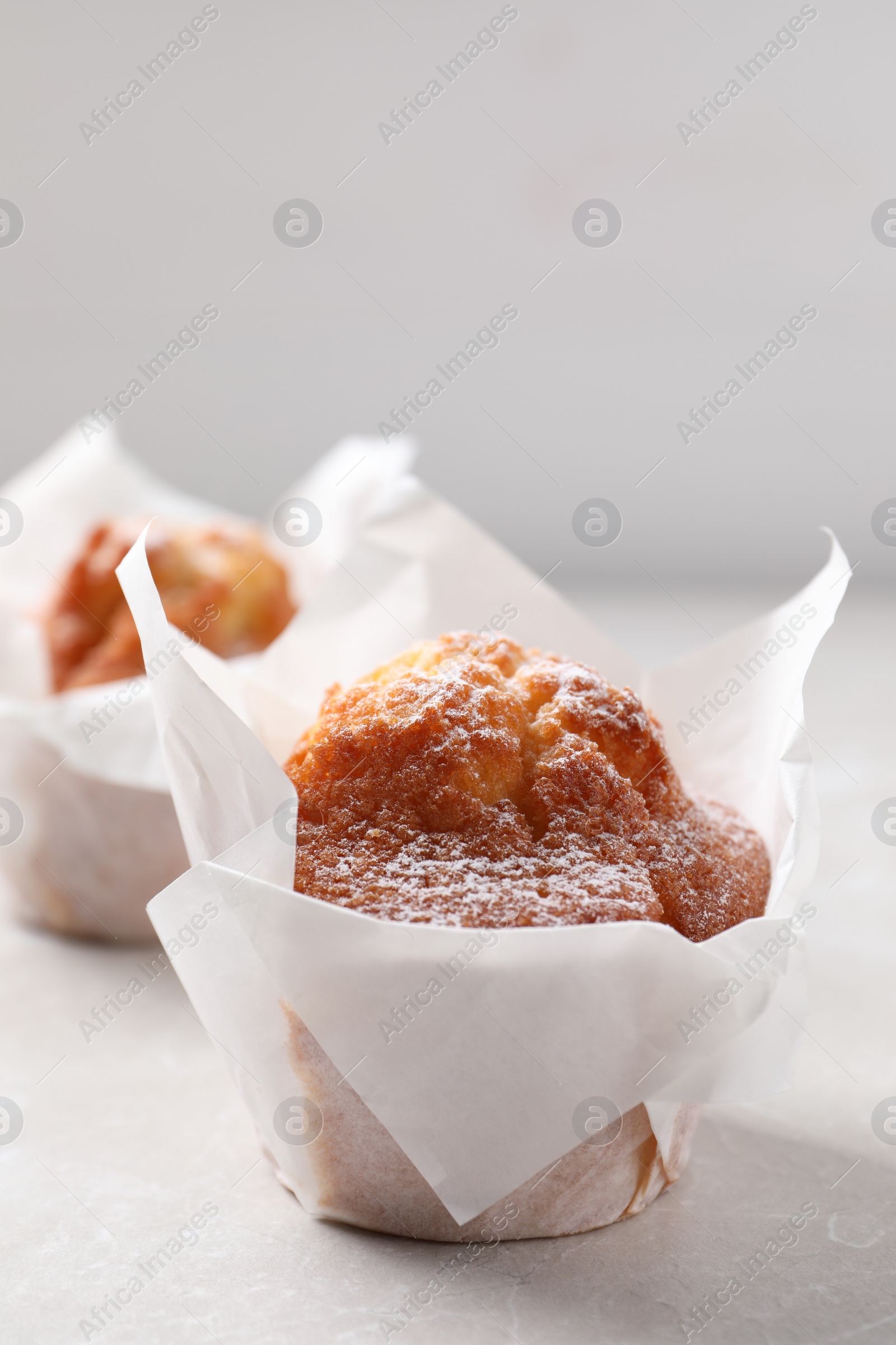 Photo of Delicious muffins with powdered sugar on light table, closeup