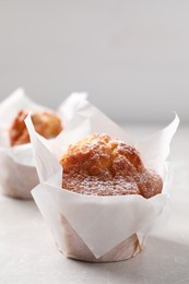 Delicious muffins with powdered sugar on light table, closeup