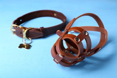 Photo of Brown leather dog muzzle and collar on light blue table, closeup