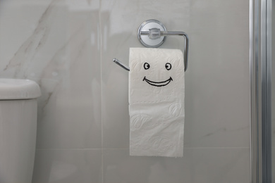 Photo of Paper with drawn funny face near toilet tank in bathroom