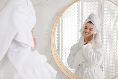 Photo of Beautiful young woman with hair wrapped in towel near mirror indoors