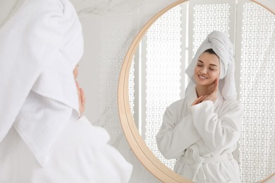 Beautiful young woman with hair wrapped in towel near mirror indoors