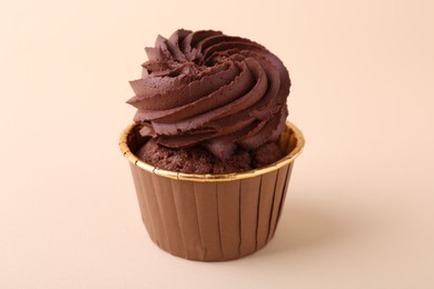 Delicious chocolate cupcake on beige background, closeup